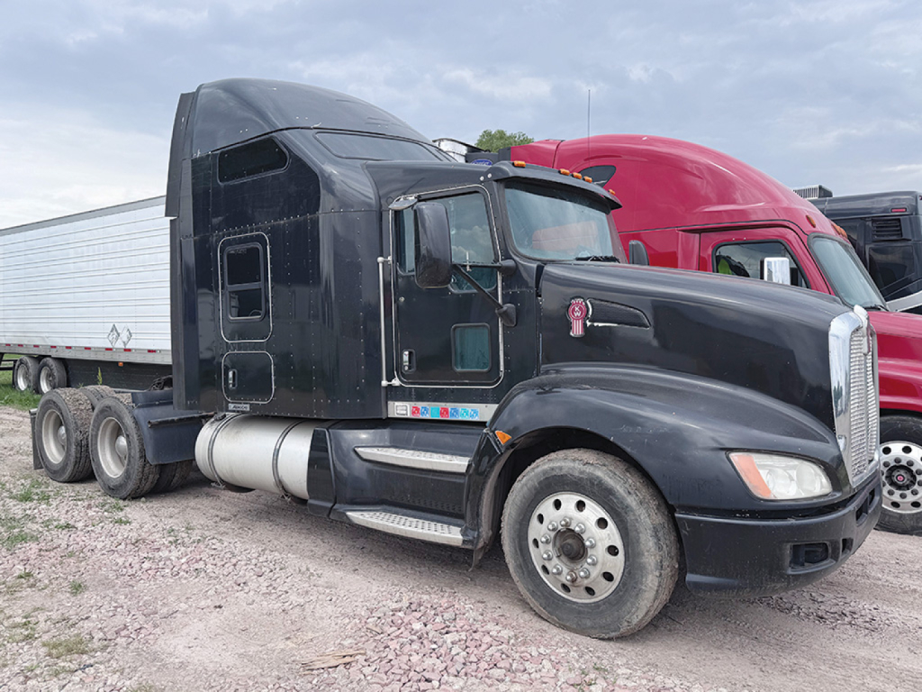 Truck cab of a 2012 Kenworth T-660 AeroCab in a used lot, black exterior, with sleeper cab and dual rear axles, side steps, fuel tanks, and wheel rims visible.