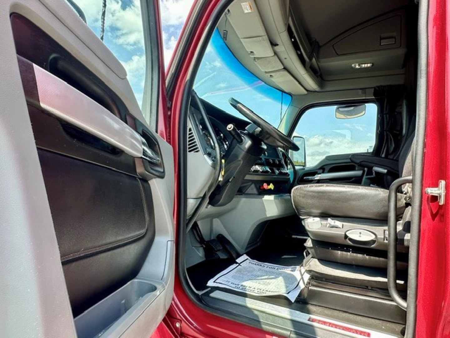Kenworth T680 truck cabin interior view from open driver door showing steering wheel and dashboard with seat controls.