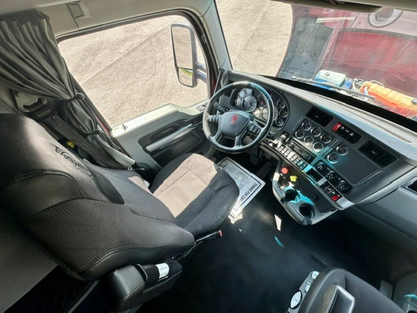 Kenworth T680 interior dashboard view showing steering wheel, front seats, and control panel with gauges and inputs.