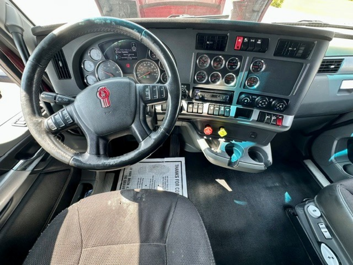 Truck cab interior of a 2022 Kenworth T680 showing steering wheel, dashboard with gauges, switches, and gear area.