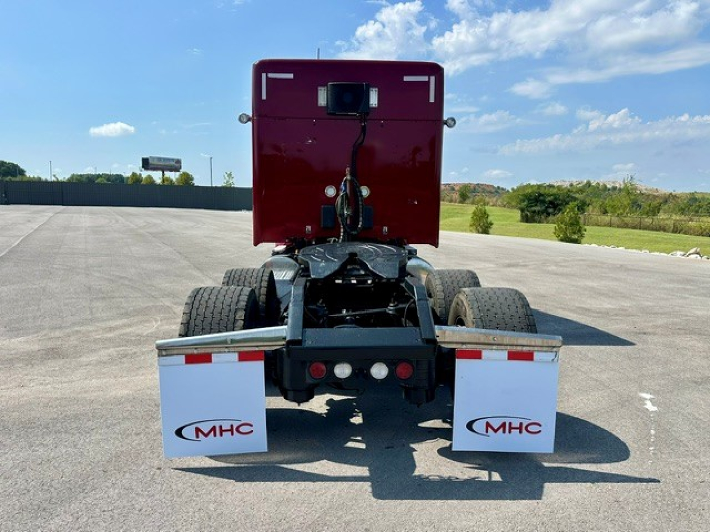 Kenworth T680 rear view focusing on the fifth wheel and rear fenders with MHC mud flaps and red sleeper cabin, clear sky in background.