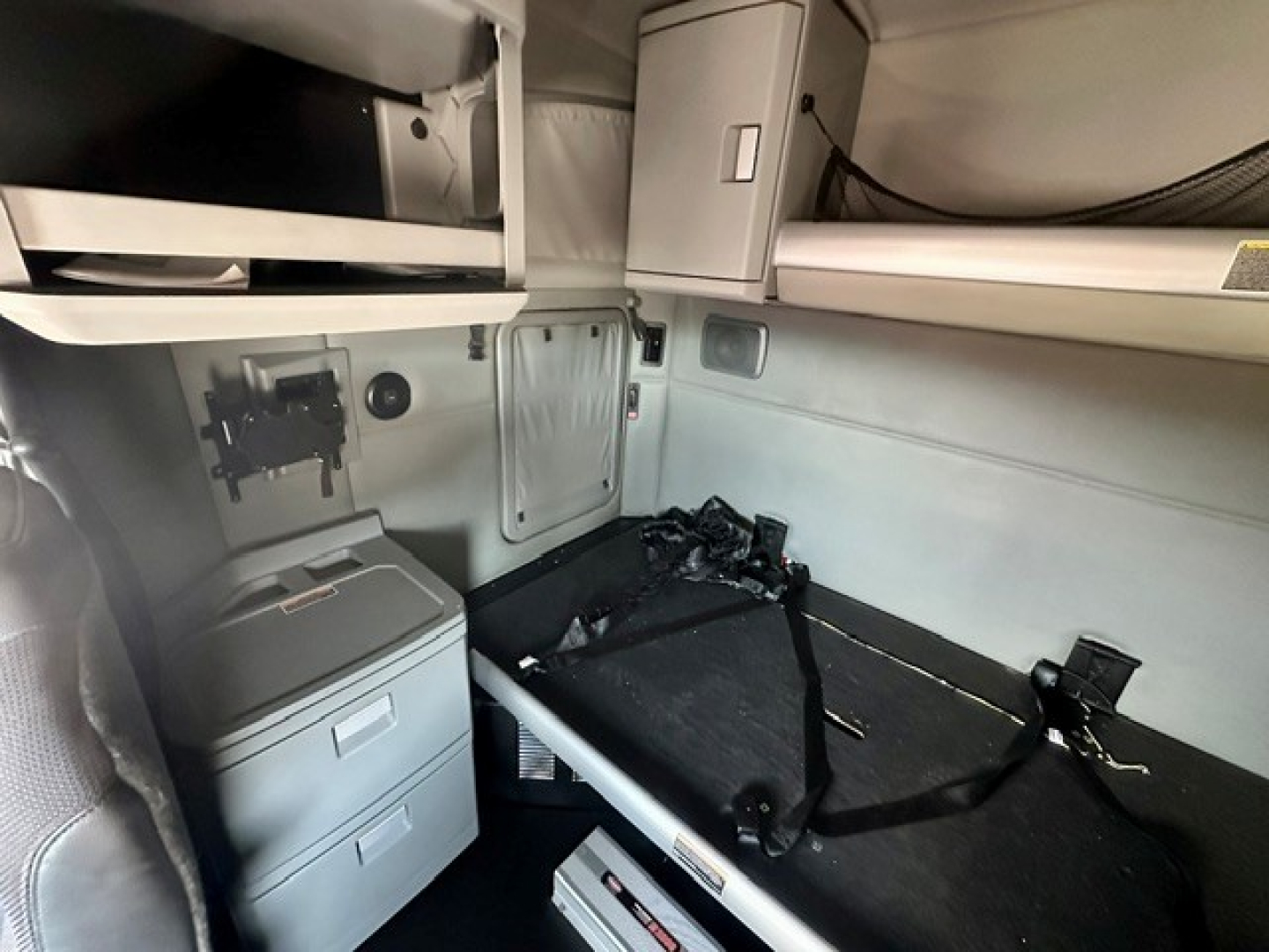 Kenworth T680 sleeper cab interior showing storage cabinet and bunk area with seatbelt and mounting hardware.
