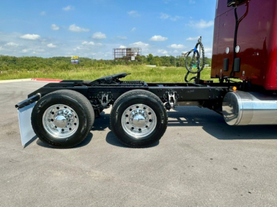 Chassis of a 2022 Kenworth T680 conventional sleeper truck showing dual rear axles and chrome wheels with fuel tank on the side.