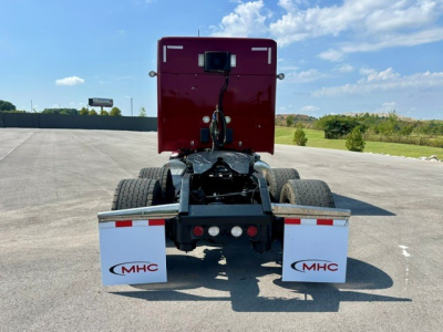 Kenworth T680 rear view focusing on the fifth wheel and rear fenders with MHC mud flaps and red sleeper cabin, clear sky in background.