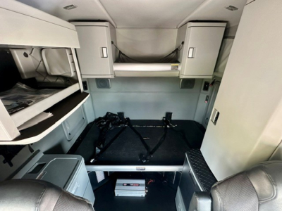 Kenworth T680 sleeper cab interior with bunk bed area, storage cabinets, and ladder steps visible.