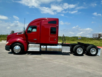 Kenworth T680 tractor cab in red, side profile view showing fuel tanks and dual rear axles.
