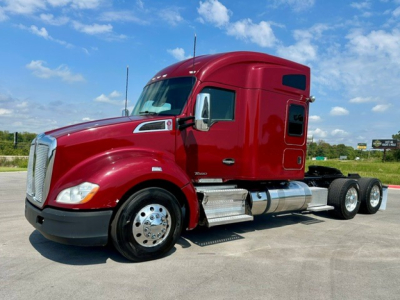 Kenworth T680 tractor unit in red, side view showing cab, front fender, chrome fuel tanks, and dual rear axles.