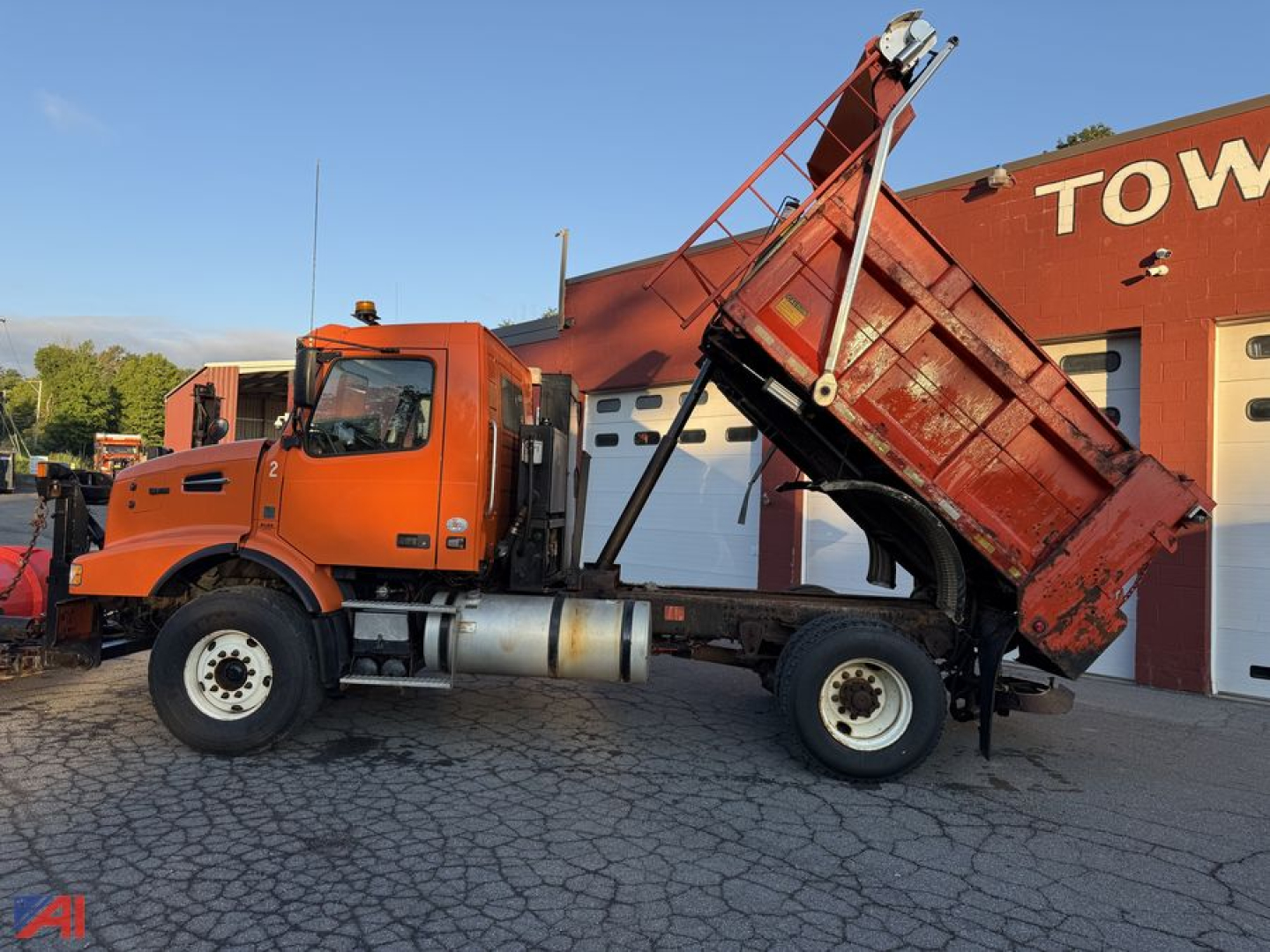 Volvo VHD dump truck with plow, side view showing orange cab and red dump bed in raised position.