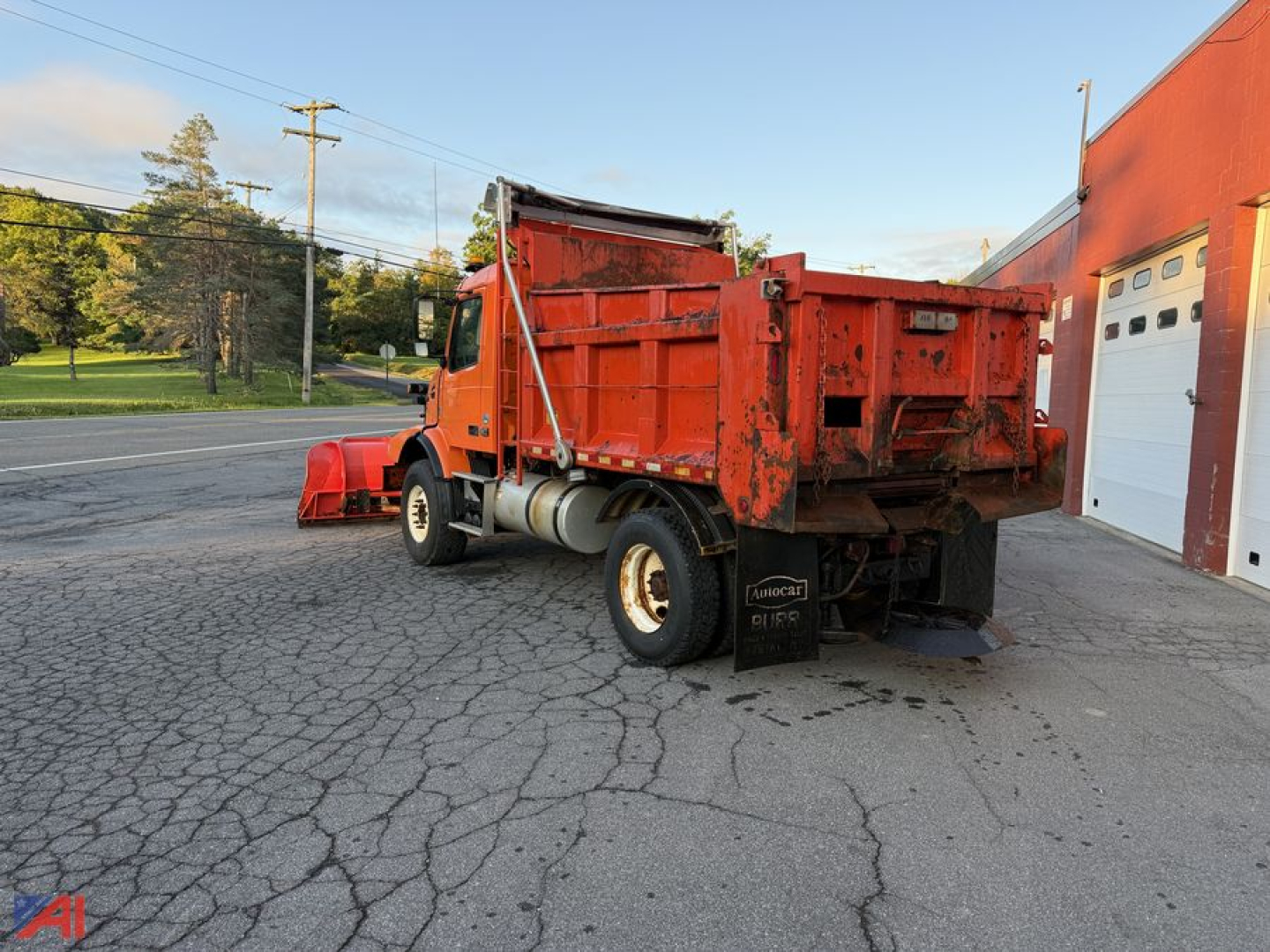 Volvo VHD dump truck with plow attached, orange body, side view showing back of truck and plow blade, VIN tag not visible.