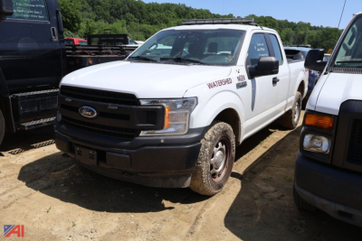 Ford F-150 pickup truck in a dirt lot, white with Waterford badge on door, front grille and bumper visible, side view showing wheel dirt