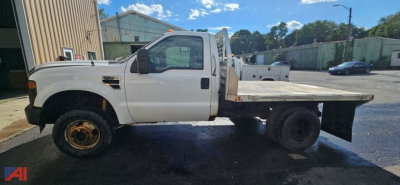 Ford F-350 Super Duty pickup with dual rear wheels seen from side, white cab, flatbed, commercial yard.