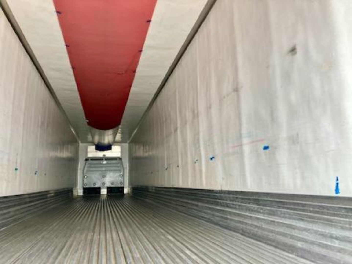 Trailer interior showing refrigerated unit access with ribbed floor and white walls, red ceiling cover, and rear cab area.
