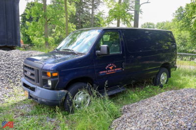 Ford E-250 cargo van in blue, side view showing front grille and wheel, used vehicle.