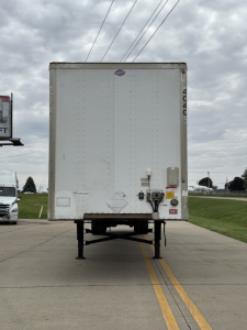 Rear view of a 2014 Utility 4000D-X trailer showing back doors, support legs, and bumper with VIN label and stickers.