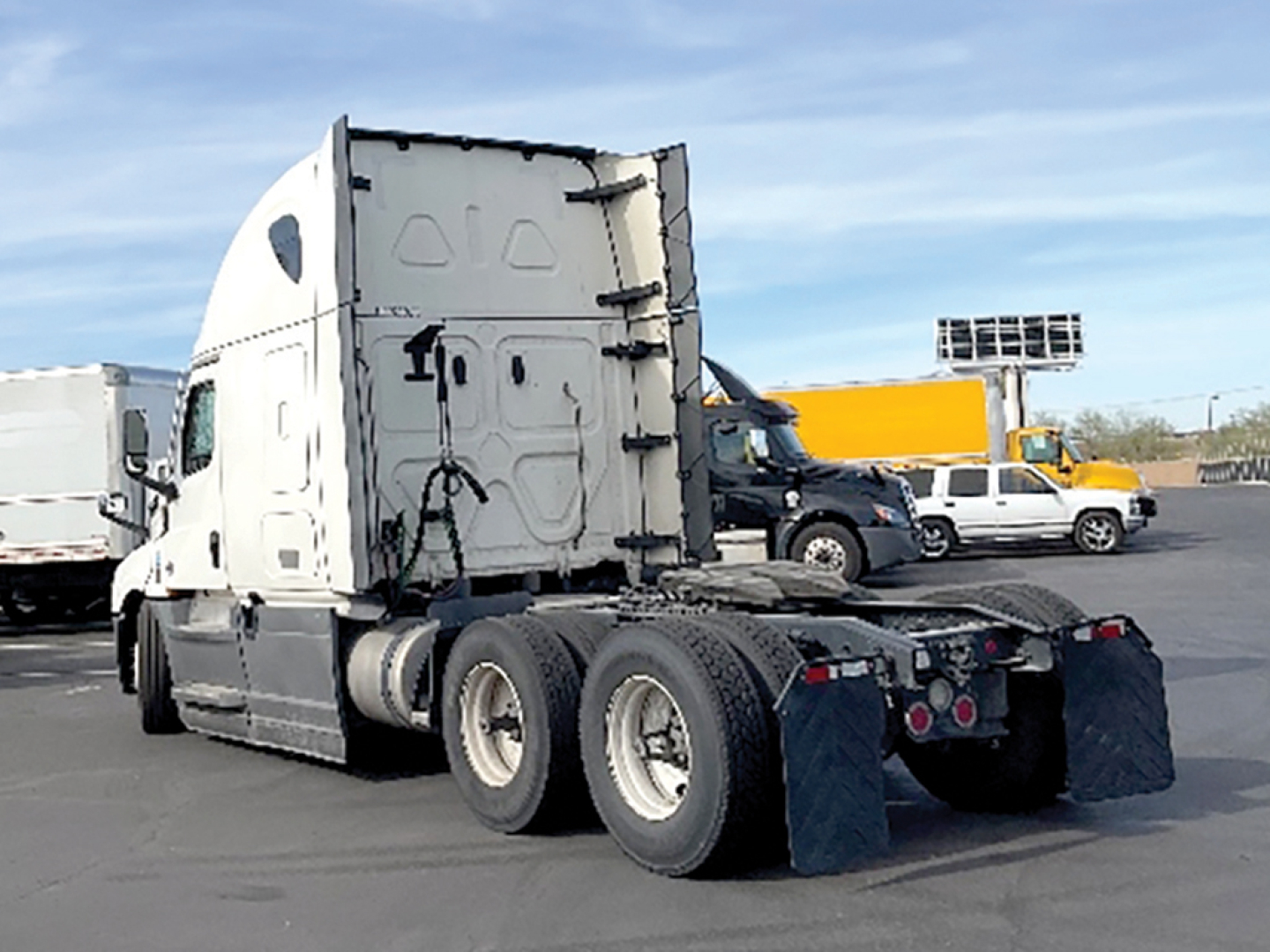 Truck rear view showing Freightliner Cascadia126 sleeper tractor with fifth wheel and dual rear axles, white cab, black chassis, mud flaps, in a dealership lot.