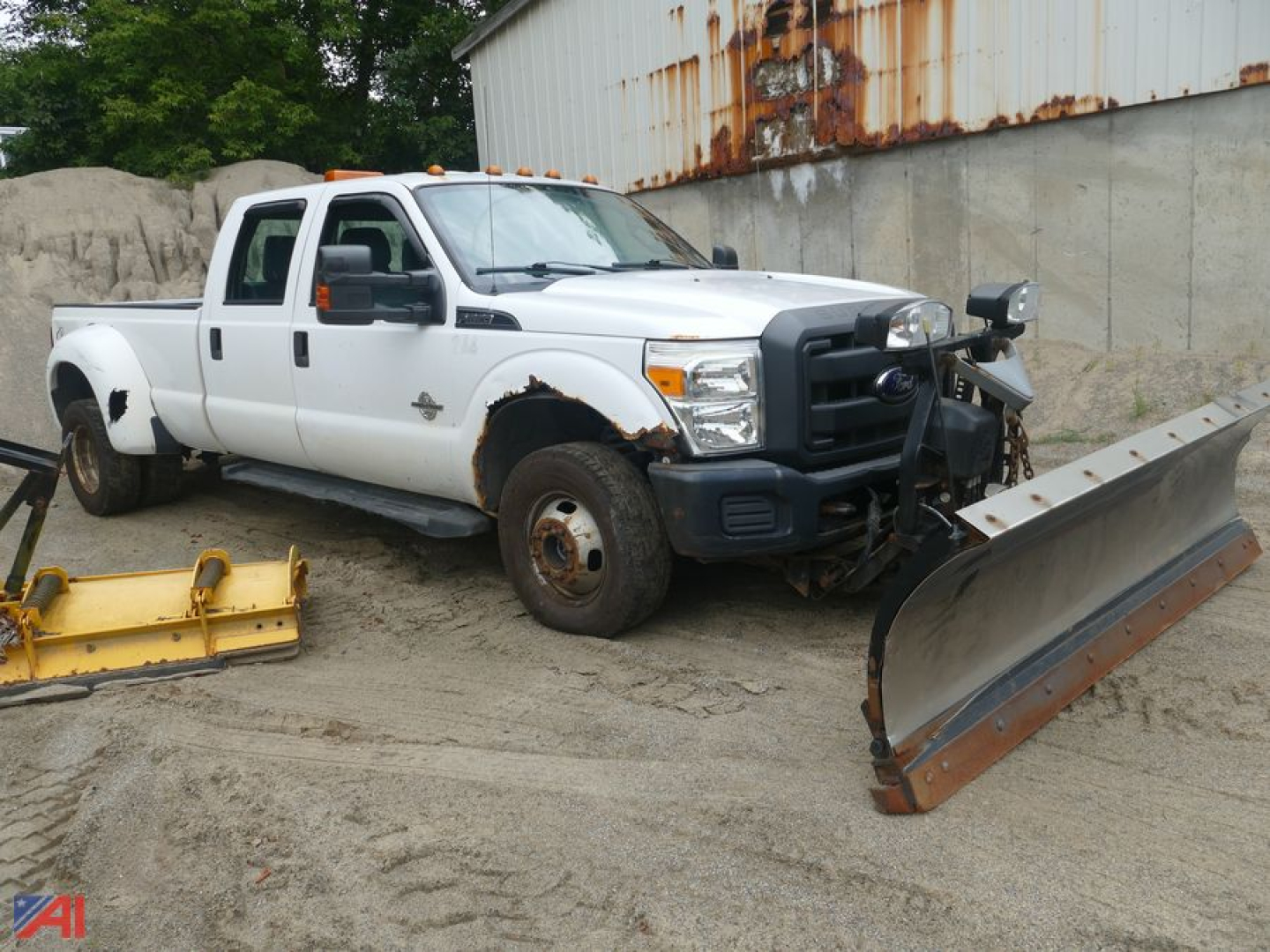 Ford F-350 Super Duty crew cab pickup with plow attachment in a yard; front bumper guard, damaged front wheel, and snowplow blade visible.