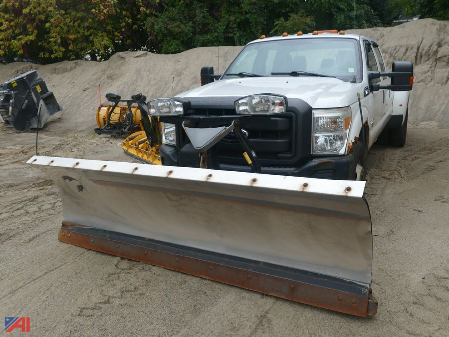 Ford F-350 Super Duty pickup with front plow attached in a dusty lot, white crew cab, dual mirrored airbags, plow blade wide and angled forward.