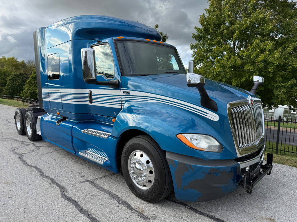 Blue 2024 International LT625 conventional sleeper truck with chrome grille and dual rear axles, side steps, and white stripe decals.