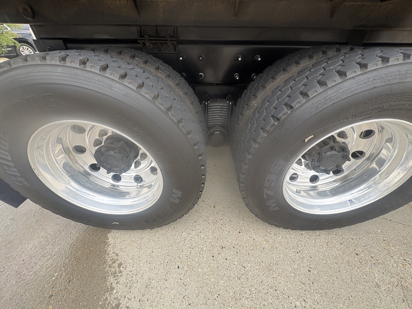 Two rear axles of a Mack GR64F dump truck with dual tires and metallic wheels; suspension springs and undercarriage visible.