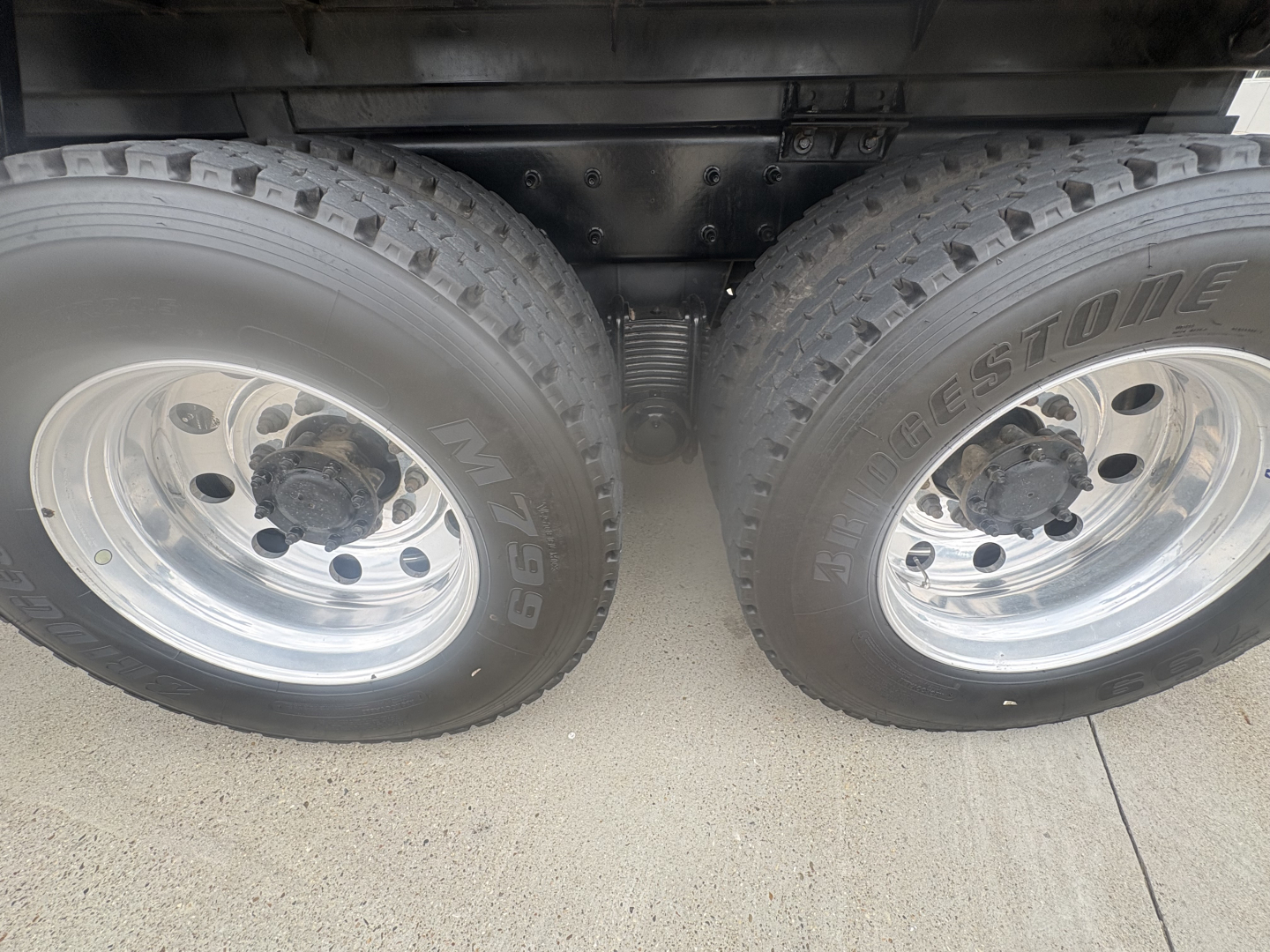 Dual rear wheels of a Mack GR64F dump truck showing Bridgestone tires and chrome rims undercarriage components.