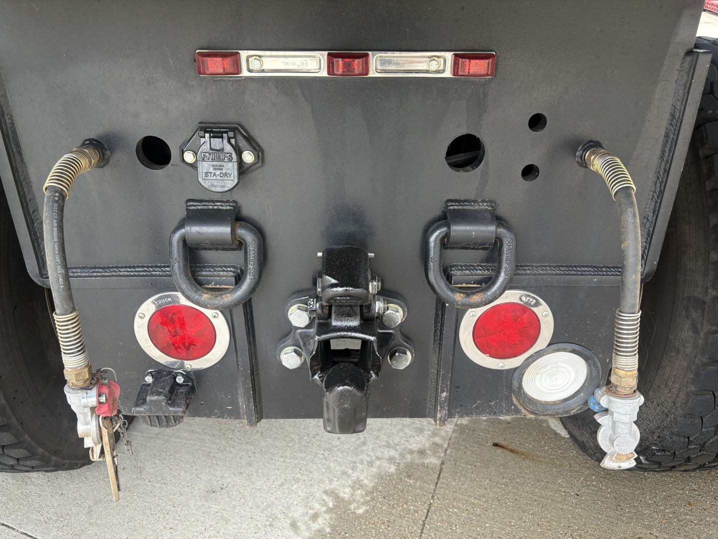 Rear view of a Mack GR64F dump truck showing hydraulic lines, taillights, hazard lights, rear hitch, and circular red reflectors with hoses and connectors.