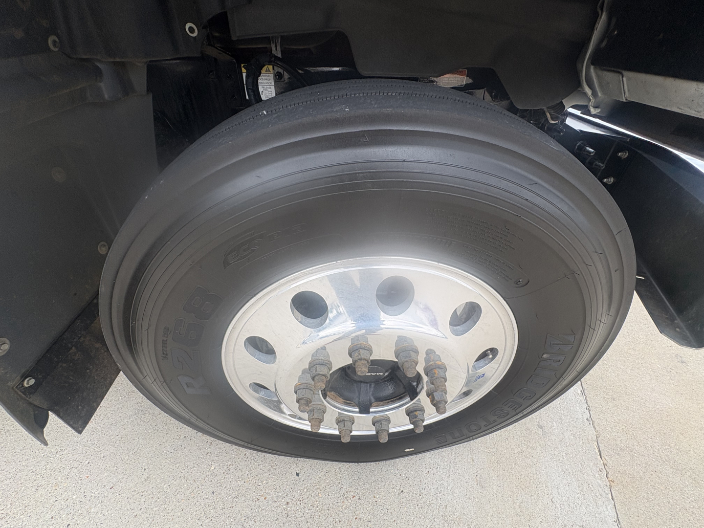 Mack GR64F wheel and tire assembly showing front axle hub and lug nuts; close-up undercarriage view with tire markings visible.