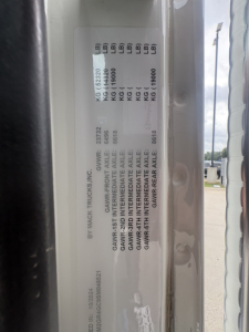 Mack GR64F dump truck door jamb label with GVWR and axle weights in kg/lb and VIN visible.