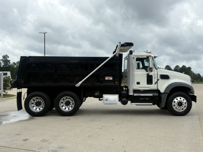 2025 Mack GR64F dump truck side view showing black dump body, white cab, multiple axles, and hydraulic dump mechanism.