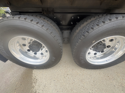 Two rear axles of a Mack GR64F dump truck with dual tires and metallic wheels; suspension springs and undercarriage visible.