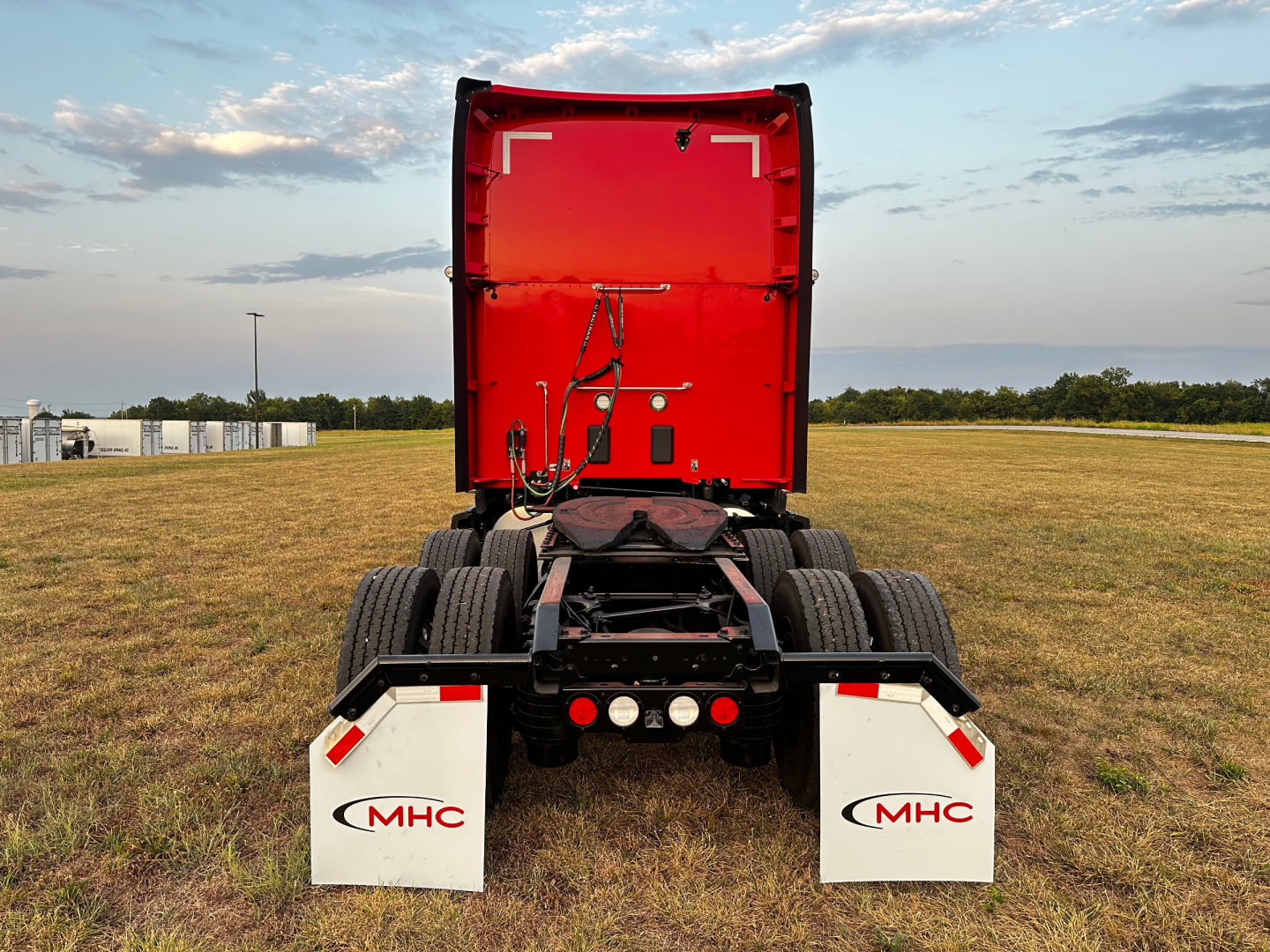Kenworth T680 rear view showing chassis, dual rear axles, red cab, white MHC mudflaps with MHC logo.