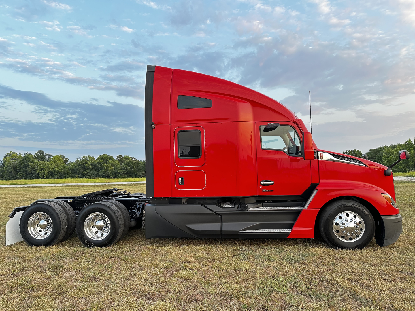 Kenworth T680 side view showing red sleeper cab, dual rear axles, chrome wheels, and chassis with no trailer.