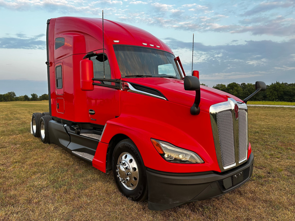 Kenworth T680 truck showing bold red exterior with aerodynamic hood and chrome grille, side mirrors, and front wheel. VIN/stock not visible in image.