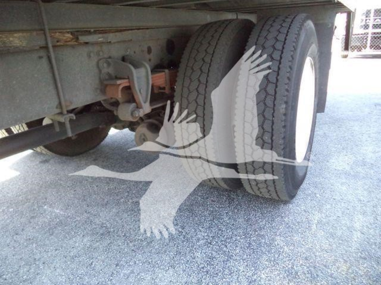Truck rear showing dual rear wheels and suspension components under a refrigerated tractor trailer.