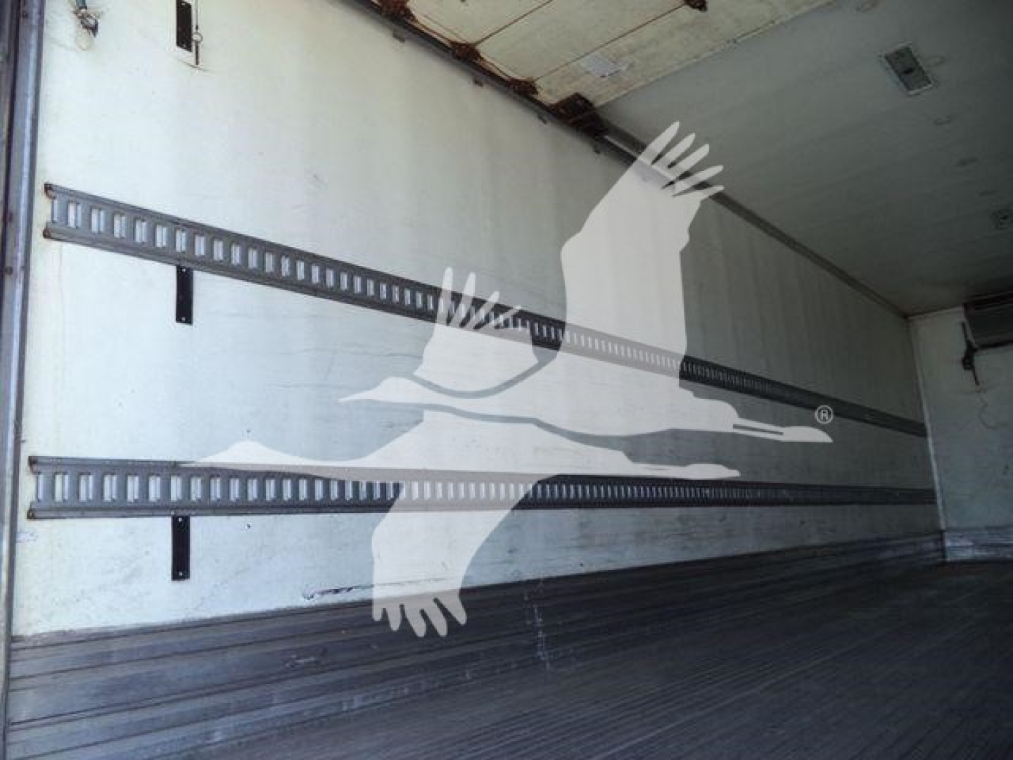 Truck trailer interior showing wall-mounted E-track rails and wooden floor, empty space.