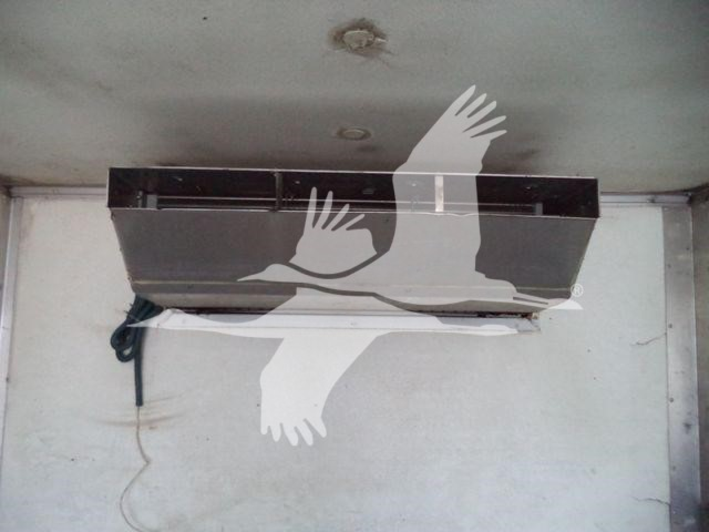 Any visible equipment: a ceiling-mounted refrigeration unit inside a truck trailer. Text visible includes no legible labels or numbers on the unit; overall view shows a dark rectangular unit with wiring on left.