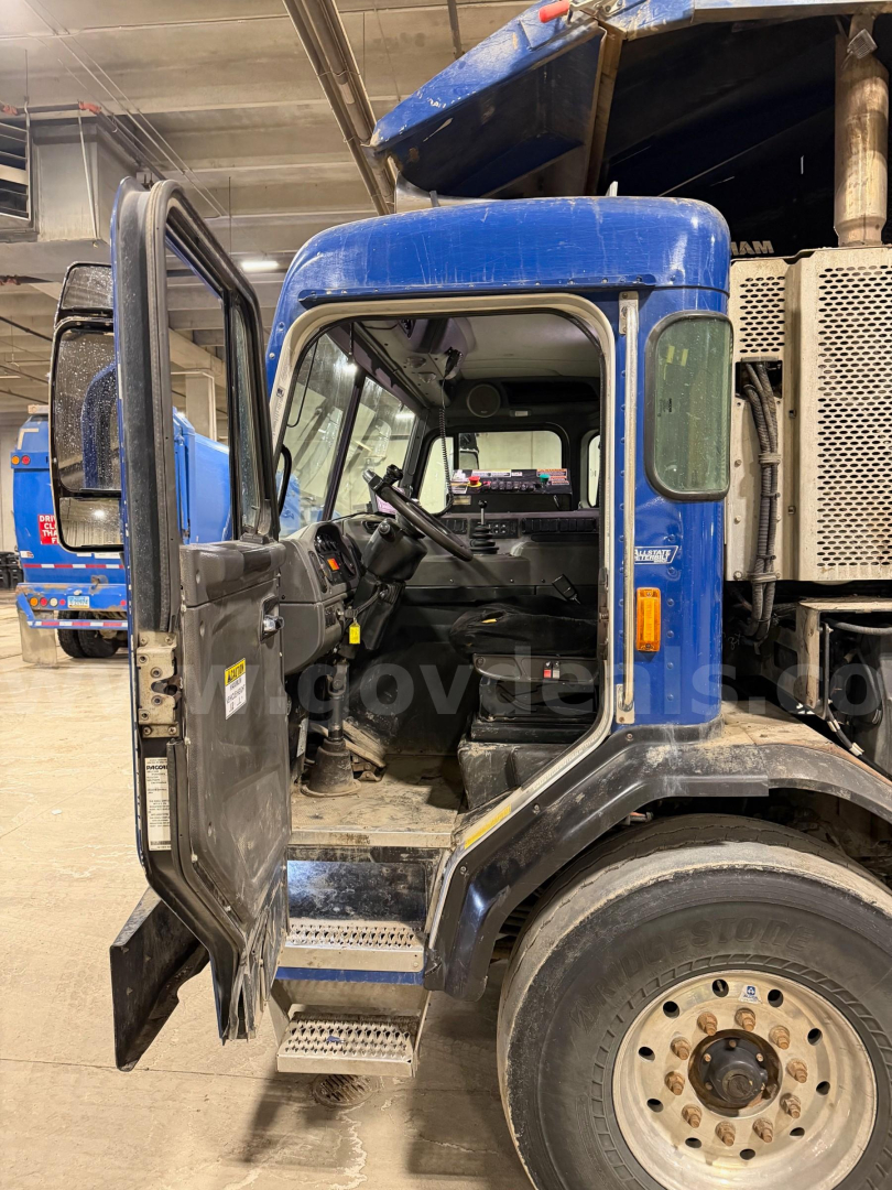 Truck cabin interior and open door of a blue 2017 Peterbilt 320 cab showing steering wheel and dashboard