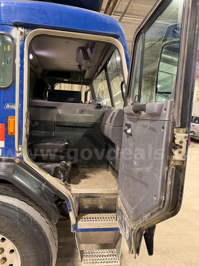 Peterbilt 320 cab interior view from open rear door showing steps and cabin with seats, vinyl floor, and dashboard edge.
