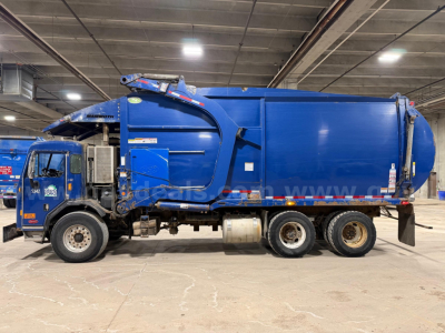 Garbage truck side view showing blue Peterbilt 320, rear compactor body, with wheels and hydraulic arms visible.