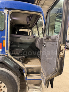 Peterbilt 320 cab interior view from open rear door showing steps and cabin with seats, vinyl floor, and dashboard edge.