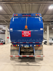Peterbilt garbage truck rear showing New Way body, tail lights, safety sign, license plate, and bumper in a warehouse.