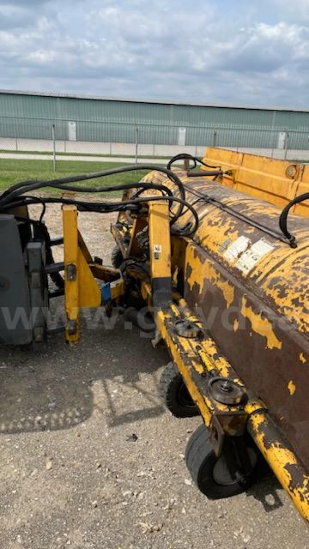 Oshkosh broom equipment with yellow hydraulic arms and peeling paint; visible hoses and joints; no legible model text.