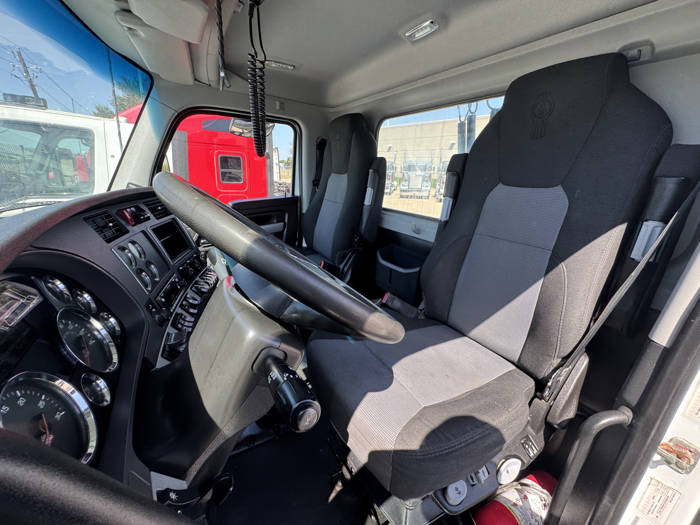 Kenworth T680 truck cab interior showing steering wheel, instrument cluster, driver seat, and passenger seat; dashboard with gauges and controls.