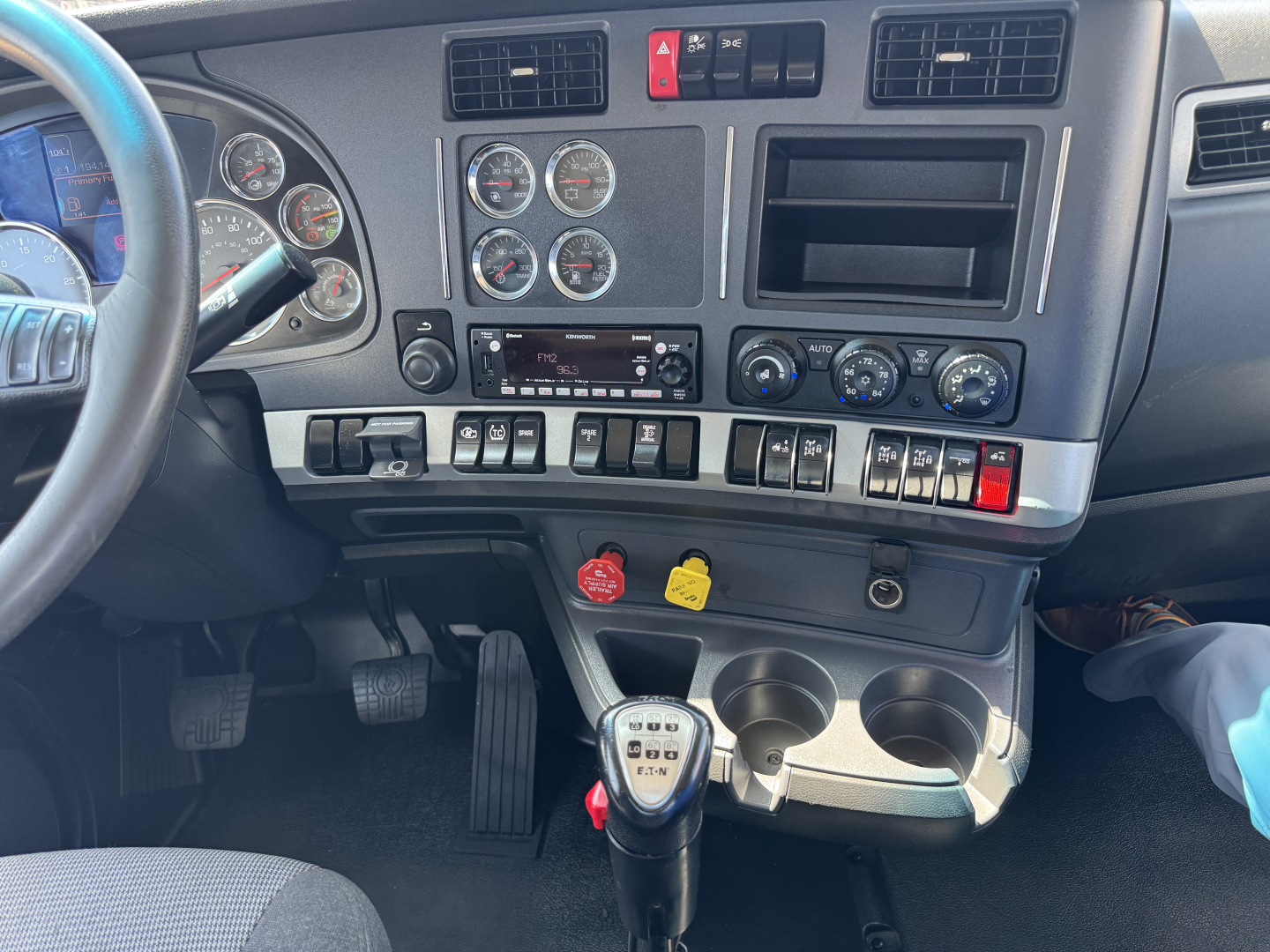 Kenworth T680 dashboard interior showing steering wheel, multiple gauges, center console with controls, gear shift, and cup holders.