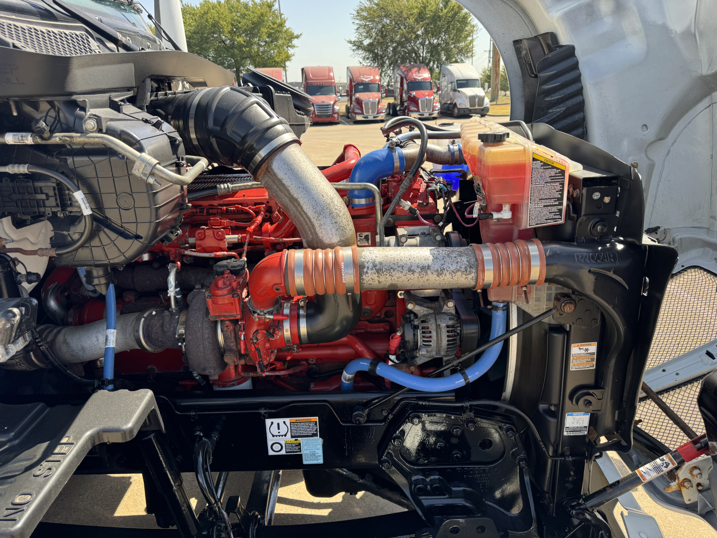 Kenworth T680 engine bay showing turbo manifold, hoses, coolant reservoir, and various engine components.