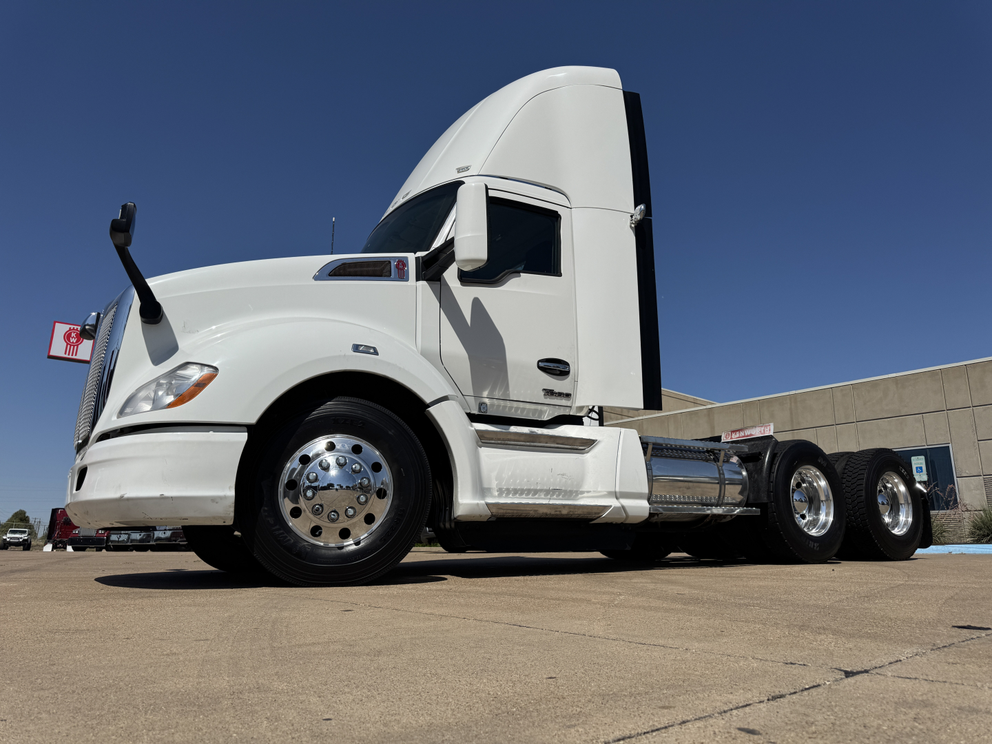 Kenworth T680 conventional day cab tractor in white, side view showing cab, fuel tanks, dual rear axles and chrome wheels.