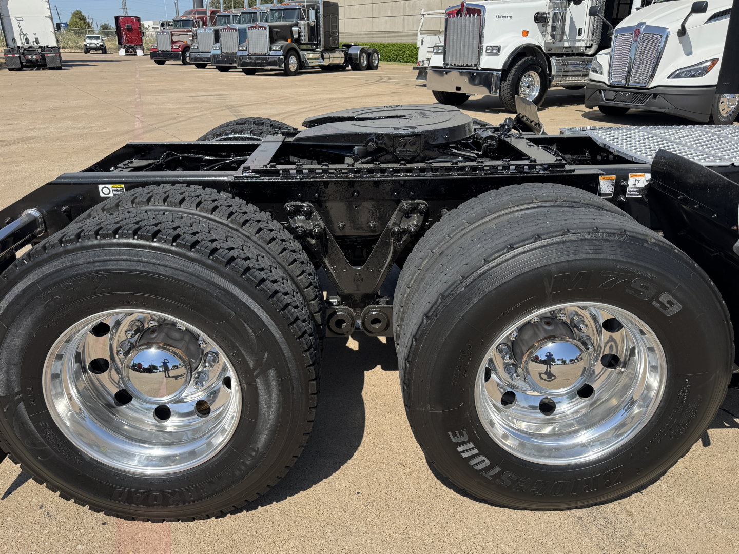 Kenworth truck chassis with dual rear axles and large tires, chrome wheels, and fuel tank area visible.