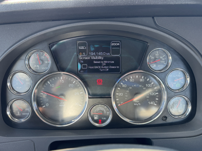 Kenworth truck dashboard showing multiple gauges and center digital display with warning prompts.