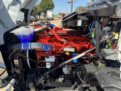 Kenworth T680 engine bay showing bright red engine block with blue coolant reservoir hose and various cables and components.