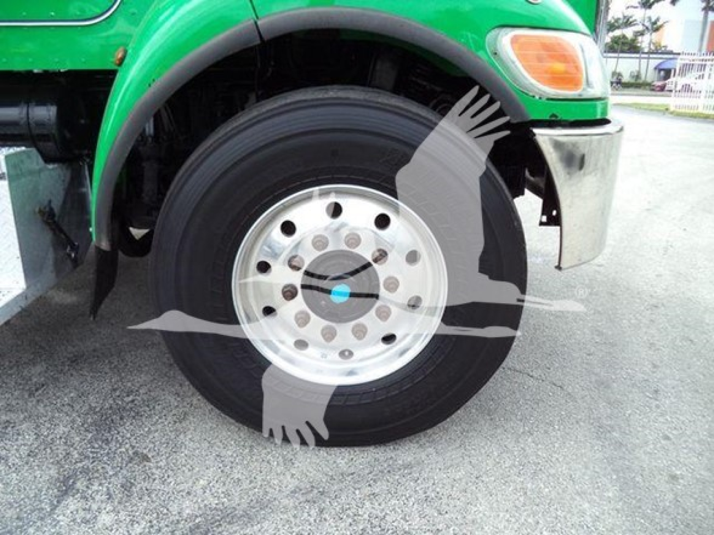 Peterbilt 348 front wheel area showing steel wheel with hub and tire, green fender, bumper, and part of front body.