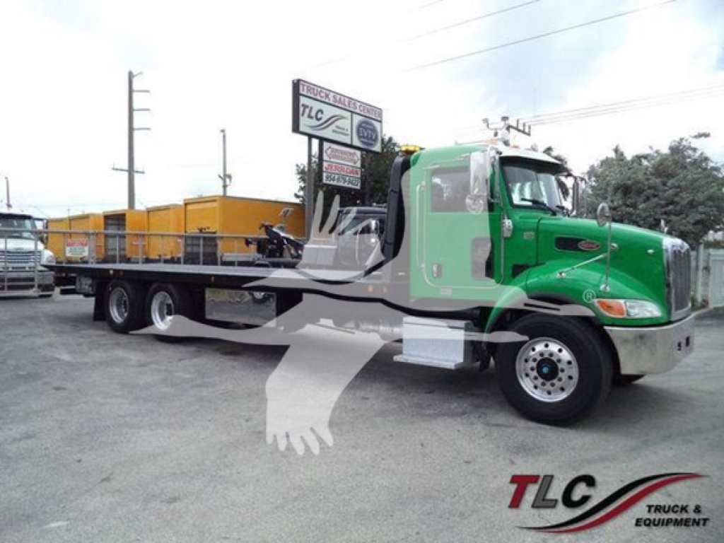 Peterbilt 348 rollback tow truck in a yard; green cab, long flatbed, chrome bumper, black chassis, DOT tires, two-tone cab with silver mirrors.
